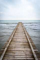 Obraz premium Wooden pier leading to the Adriatic Sea on a cloudy autumn beach in Italy
