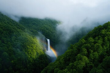 aerial view of a stunning waterfall cascading down a lush green mountainside with a rainbow and fog