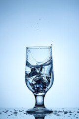 Refreshing splash of ice in a crystal-clear glass under serene blue backdrop