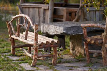 Naklejka premium A fragment of the tourist infrastructure of the Elbrus region. Homemade table with benches made of logs by the pond in harmony with the surrounding rocky mountains.
