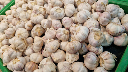 Garlic close up in supermarket. Lots of garlic in plastic green box on market stall. Garlic in green plastic box at farmers market. Garlic for sale in store. Display of fresh produce for sale