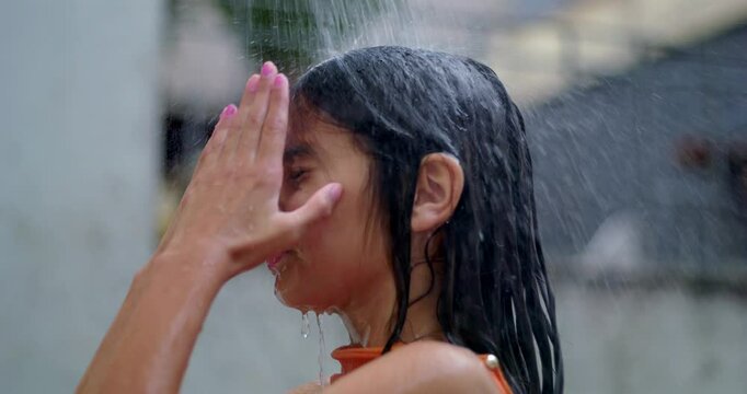 Young girl under an outdoor shower on a summer day, smiling softly with eyes closed, embracing a tranquil and refreshing moment in a diverse and carefree setting