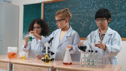 Children doing experiment in science lesson while standing at blackboard at laboratory. Happy student discovering and learning about biochemical liquid while inspecting and mixing sample. Pedagogy.
