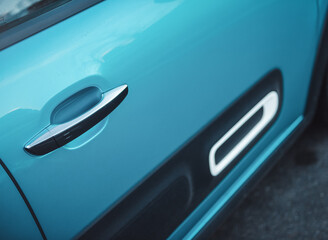 Close up of a door handle of a teal car. Exterior car door handle on the front door.