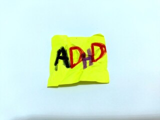 A yellow paper note with the abbreviation ADHD on it isolated on white background. Close up. ADHD...