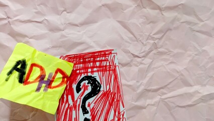 The words ADHD on crumpled yellow paper and a black question mark with red around it drawn on...
