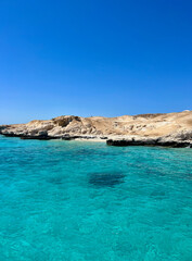 Bright blue skies surround the serene turquoise waters, gently lapping against rocky cliffs in Egypt. The clear sea reflects sunlight, creating a stunning coastal view.