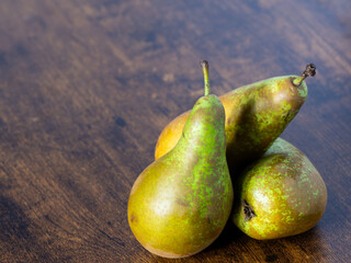 Three green pears are sitting on a wooden table. The pears are ripe and ready to eat