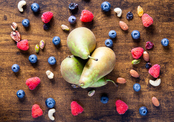 A bowl of fruit with pears and blueberries on top of a wooden table. The fruit is scattered around the table, with some of it being in the foreground and some in the background