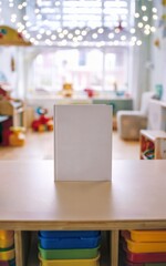 Blank White Book Standing on a Table in a Colorful Playroom

