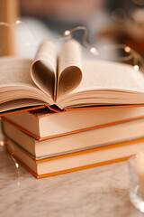 Folded paper book pages in heart shape over glowing lights close up. Valentines Day.