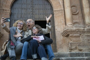 Group of senior tourists taking a joyful selfie on the steps of a historic Spanish church during a...