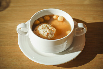 A steaming bowl of soup with a bacon dumpling and small croutons served in a white dish on a wooden surface. The image captures a cozy, warm, and appetizing atmosphere.