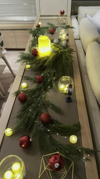 A festive Christmas table centerpiece with evergreen garland red ornaments LED candles and warm fairy lights creating a cozy holiday ambiance concept of holiday decor interior design event planning