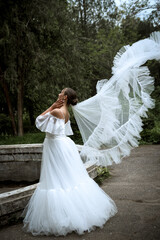 beautiful bride with long veil against the background of trees and old fountain.
