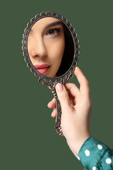 Beautiful woman looking in handheld mirror on dark green background, closeup © New Africa