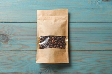Paper pouch bag with coffee beans on light blue wooden table, top view