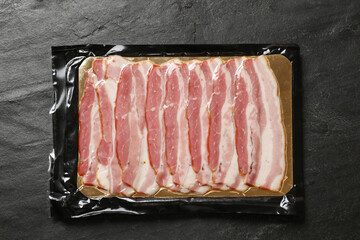 Pack of sliced bacon on black table, top view