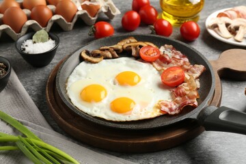 Tasty fried eggs with bacon and mushrooms served on grey table, closeup