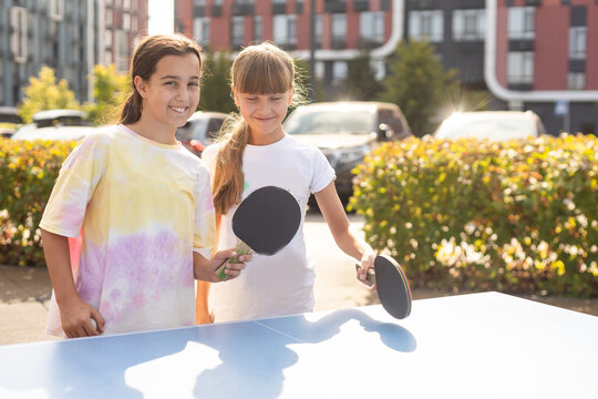 Young teenager girl playing ping pong. She holds a ball and a racket in her hands. Playing table tennis outdoors in the yard