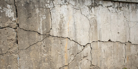 A weathered concrete wall shows multiple cracks and discolorations, revealing its aging surface. The texture highlights the effects of time and environmental factors