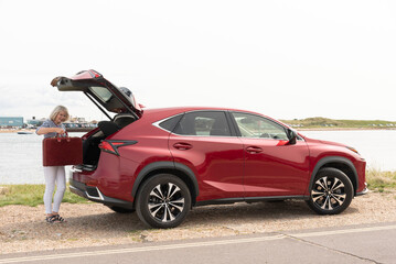 Southsea Portsmouth England UK. 28.08.2024.  Elderly lady unloading suitcase from boot of her car at a seaside resort in southern England UK.