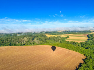 Obraz premium The shadow of the hot air balloon falls on the fields of wheat, at the level of the clouds. Europe, Czech Republic