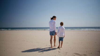 Woman boy walking beach holding hands at summer holidays. Mother strolling son