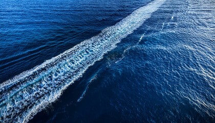 aerial view of ocean water wake pattern left by a boat showing turbulent waves and trail on deep blue sea surface
