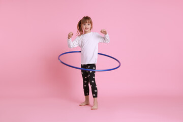 Cute little girl exercising with hula hoop on pink background