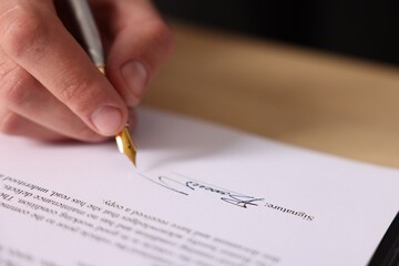 Man putting signature on document at table, closeup