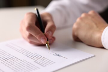 Fototapeta premium Man putting signature on document at white table, closeup