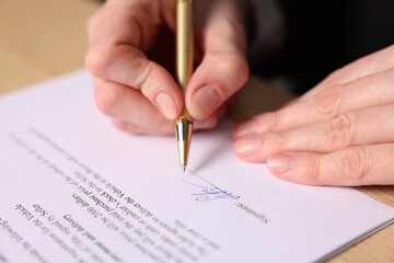 Woman putting signature on document at table, closeup