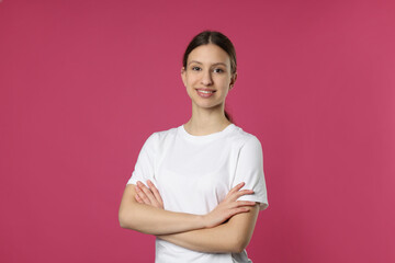 Obraz premium Portrait of smiling teenage girl with crossed arms on pink background