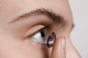 Woman putting in color contact lens on light background, closeup