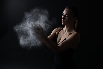 Woman clapping hands with talcum powder before training on black background