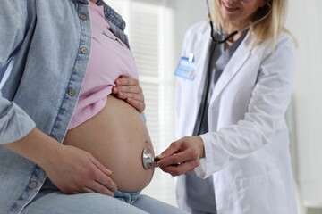 Pregnancy checkup. Doctor with stethoscope listening baby's heartbeat in patient's tummy indoors,...