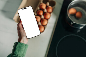 woman hand in a green shirt holds a mobile phone above eggs in the kitchen