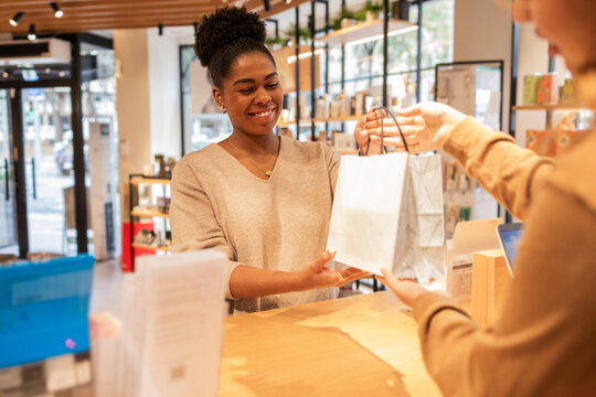 Smiling assistant handing a bag in a cosmetics store setting