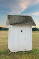 A white outhouse standing behind house in a field © Rix Pix