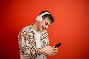 young boy with headphones studio shot on red background use cellphone