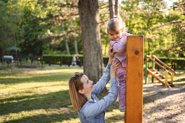 Obraz premium Smiling mom helps her cute daughter climb the playground