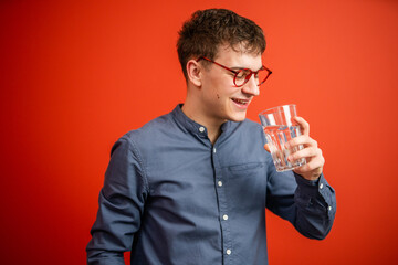 portrait of young man drink water in front red background studio shot