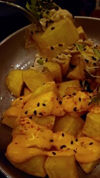 Patatas bravas are served with black garlic aioli, sesame seeds, and chili flakes