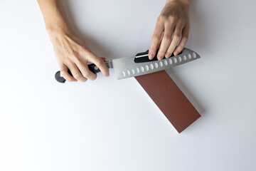 on white background on a table, women's hands sharpen a steel knife, a lock under the arm,...