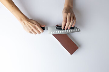 on white background on a table, women's hands sharpen a steel knife, a lock under the arm, protection against cuts, a red medium-hard stone for sharpening knives