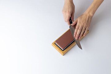 top shot on white background on a table, women's hands sharpen a steel knife, a lock under the arm, protection against cuts, a red medium-hard stone for sharpening knives