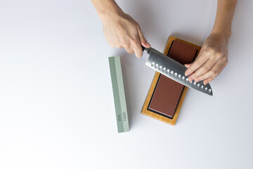 top shot on white background on a table, women's hands sharpen a steel knife, a lock under the arm, protection against cuts, a red medium-hard stone for sharpening knives green whetstone nearby