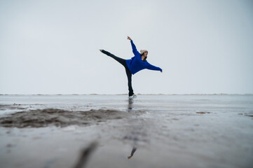 Caucasian woman in a blue sweater is skating on a frozen lake. Figure skater performs a swallow. 