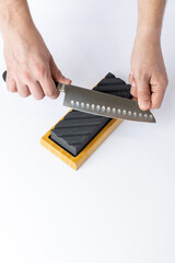 close up on white background on a table, man hands sharpen a steel knife protection against cuts, a...